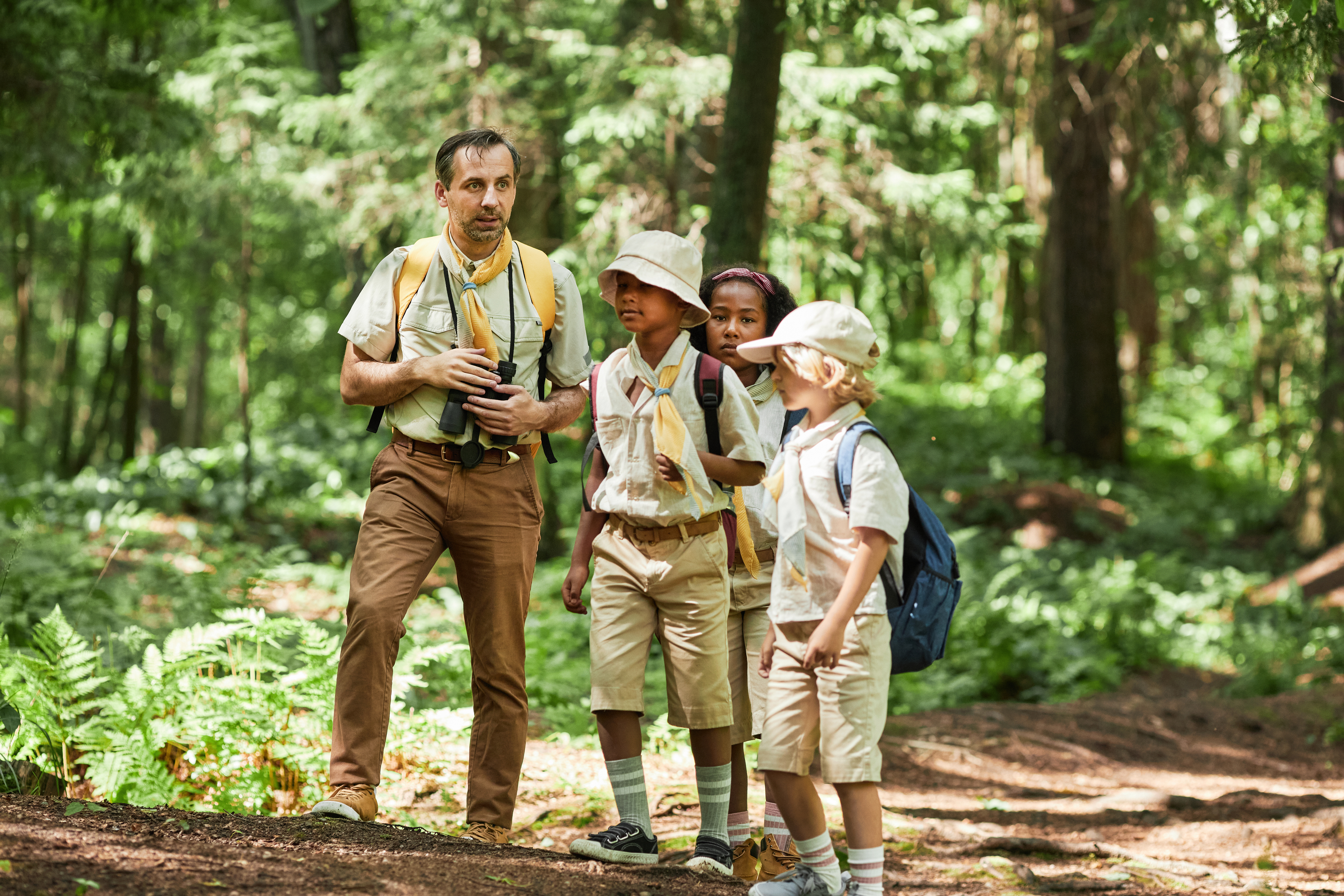 Picture of three children with an adult holding bincoculars walking in a forest