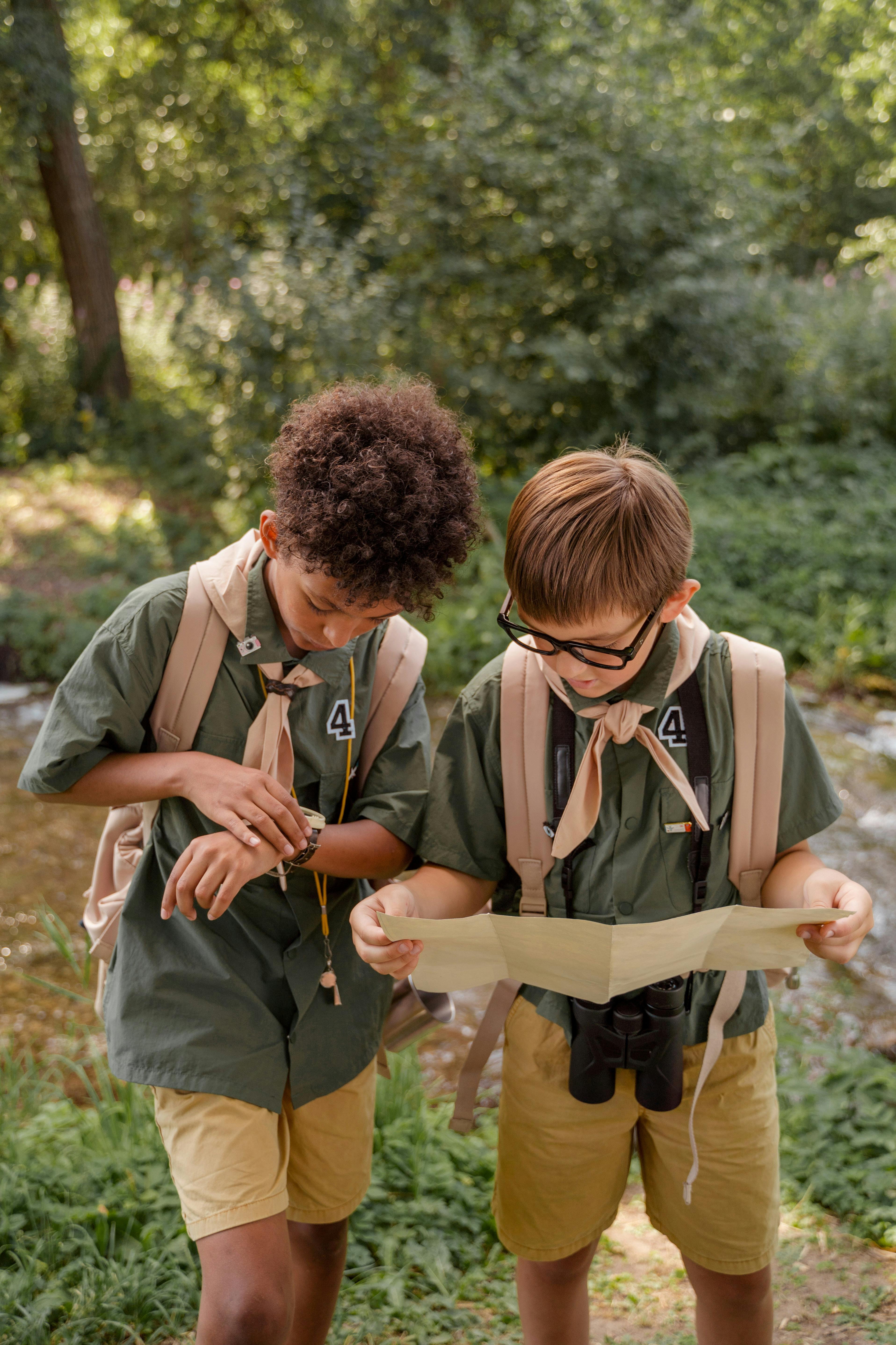 two boys standing in a forest looking at a map and a watch