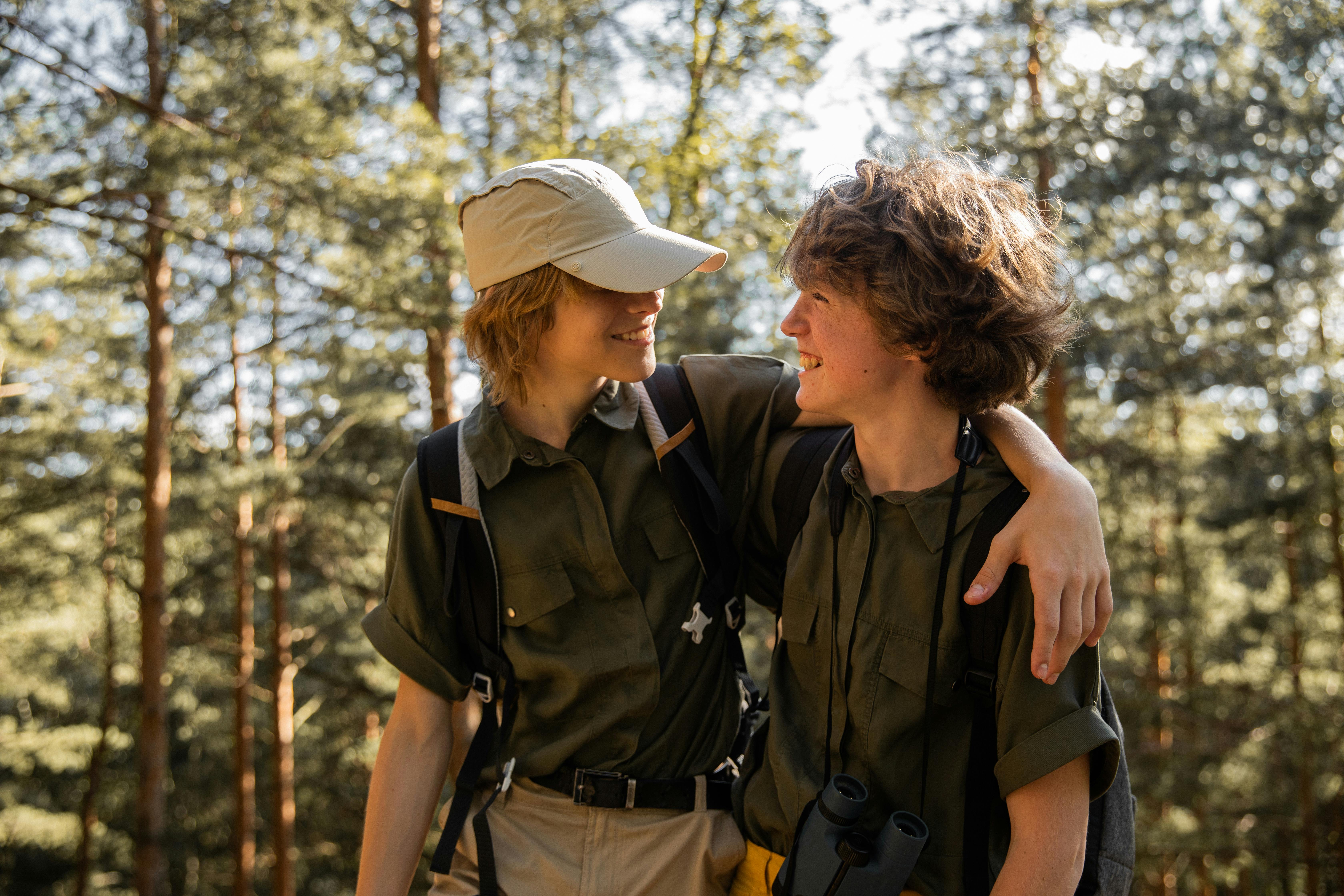 two teenage boys hugging and looking at each other standing in a forest